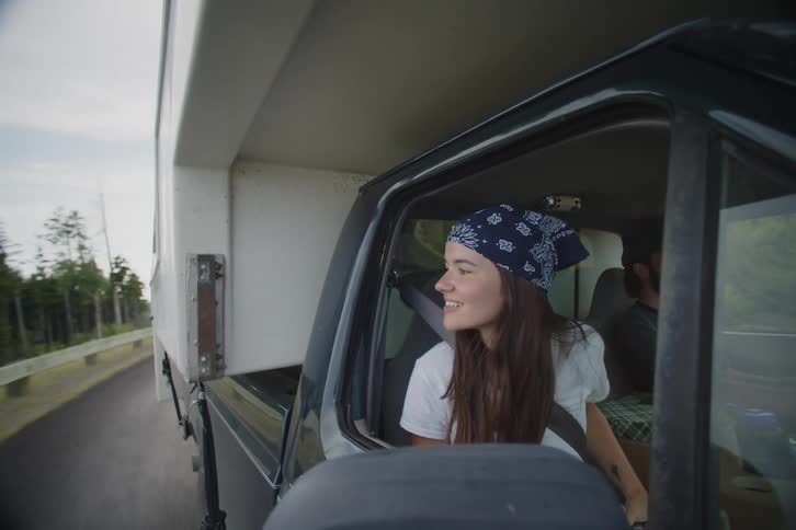Woman in the passenger seat of a traveling truck holds a video camera out of the window