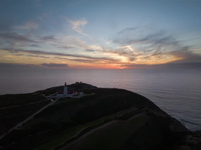 Aerial view of a lighthouse on a rocky coastal point overlooking the ocean at sunset