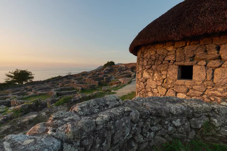 The sun sets upon a small stone building on a hill above the coast