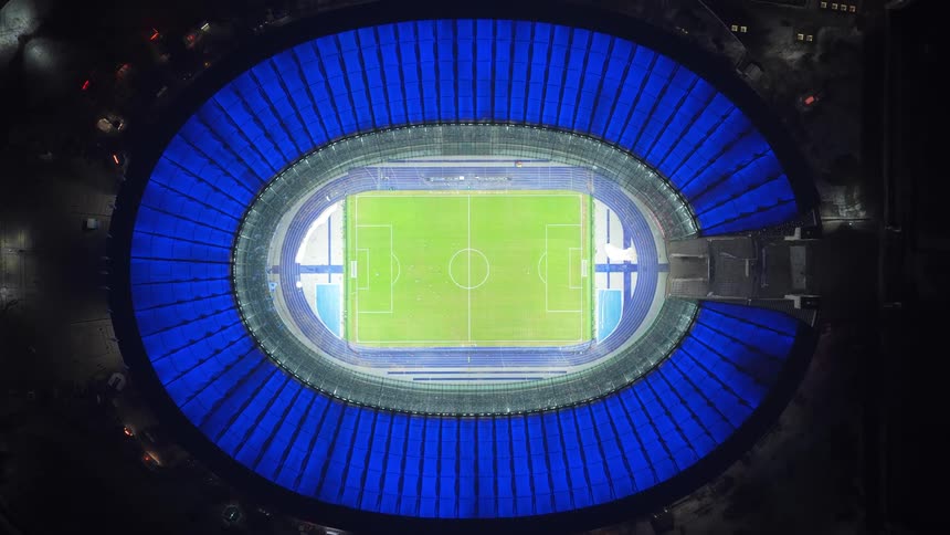 Illuminated oval stadium seen from above with a football pitch in the center