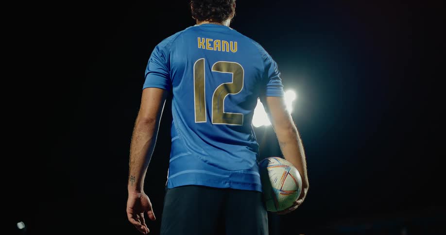 Back of a man wearing a numbered jersey standing inside the stadium at night with a ball in his hand