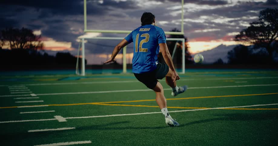 Player wearing blue number 12 jersey kicking a ball toward the goal on a sports field