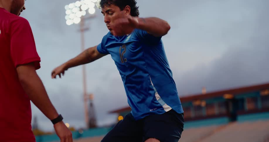 A soccer player in a blue jersey chesttraps a ball while facing an opponent in a red jerseythe action moves to a lowangle shot of their feet as they move across the green turf during the drill