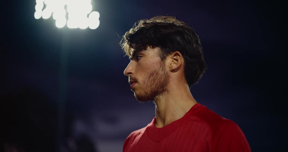 A football player standing on a field at night wearing a red jersey