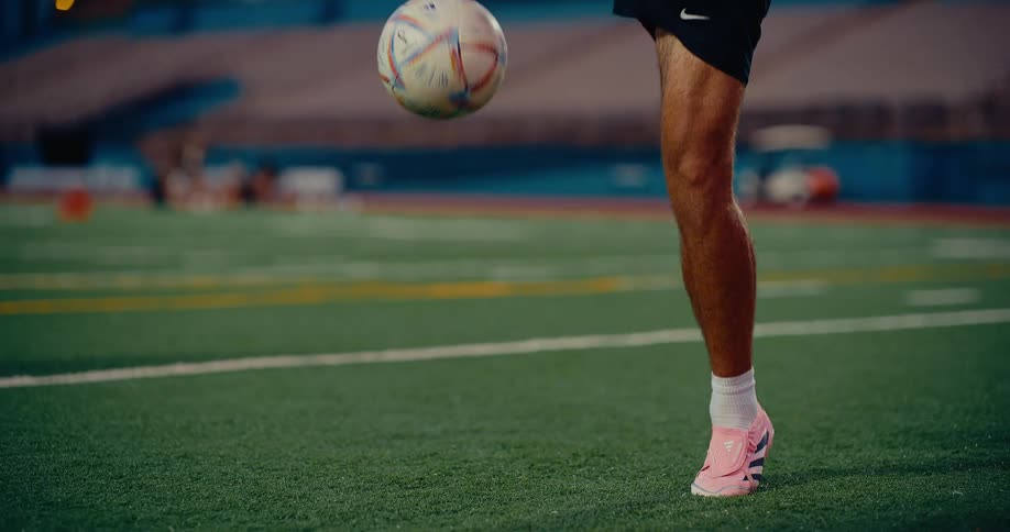 A soccer player wearing pink cleats practices juggling a ball on an athletic field the video shows a closeup of their legs and feet as they maintain control of the ball in the air