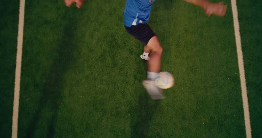 An overhead view captures a soccer player striking the ball his leg swinging powerfully across the bright green turf