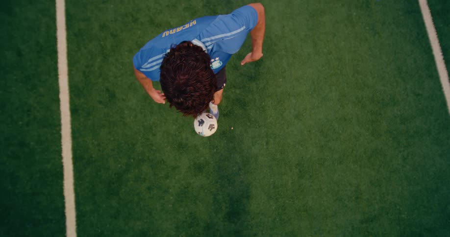 Aerial of a man juggling soccer ball on the grass field at night