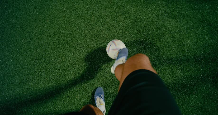 One soccer player stands in front of another who is lightly kicking the ball