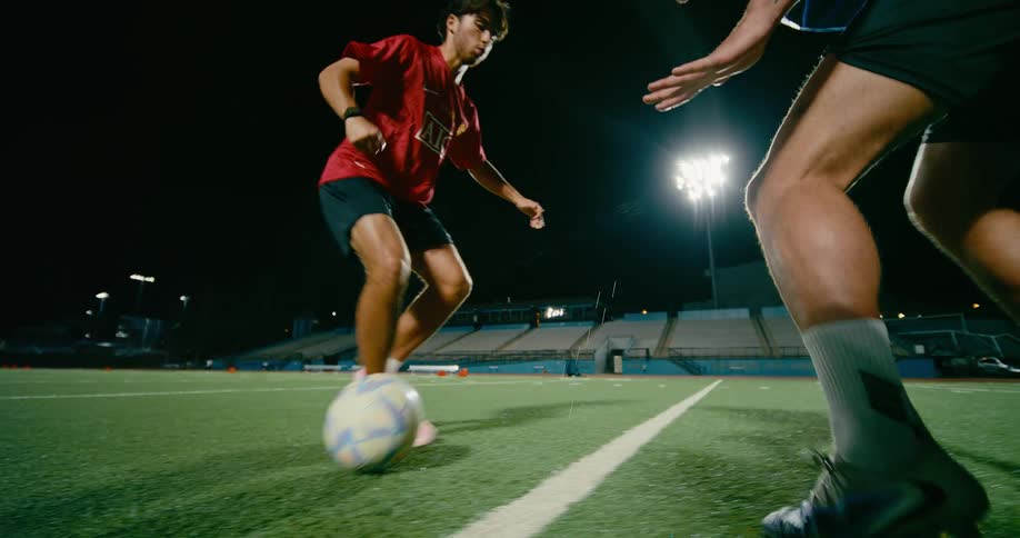 Two soccer players play one on one on an urban sports field at night