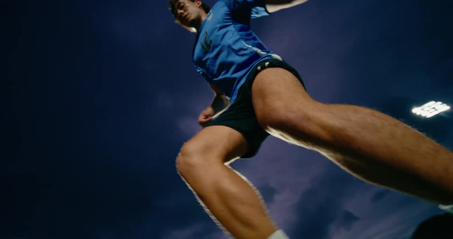 Male athlete practices dribbling on a sports field at night