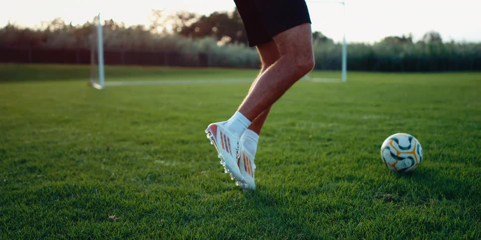 A soccer player kicks a ball on a green field at sunset