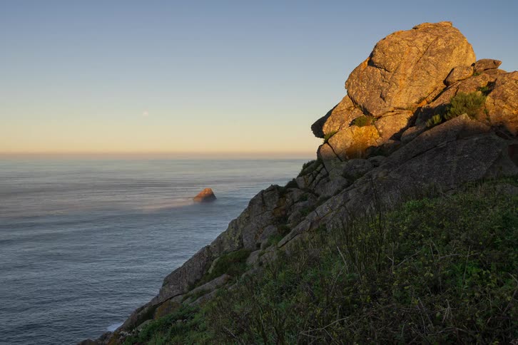 Woman climbs up onto and down from a coastal rock formation in the morning