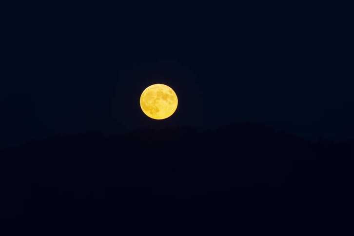 Full moon rising over a mountain in the night sky