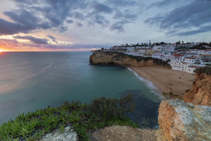 A time lapse of the sun setting over a coastal town with a beach nearby