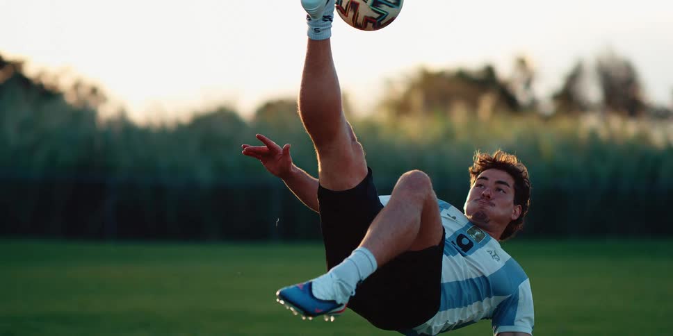 Young male soccer player performs a bicycle kick on the soccer ball while near sunset in the summer