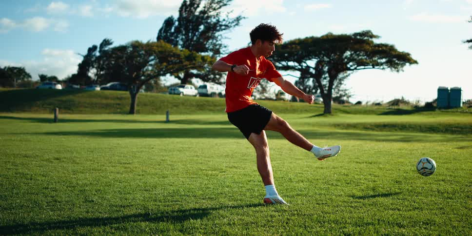 Male soccer player playing at the park kicks a soccer ball on a cloudy summer day