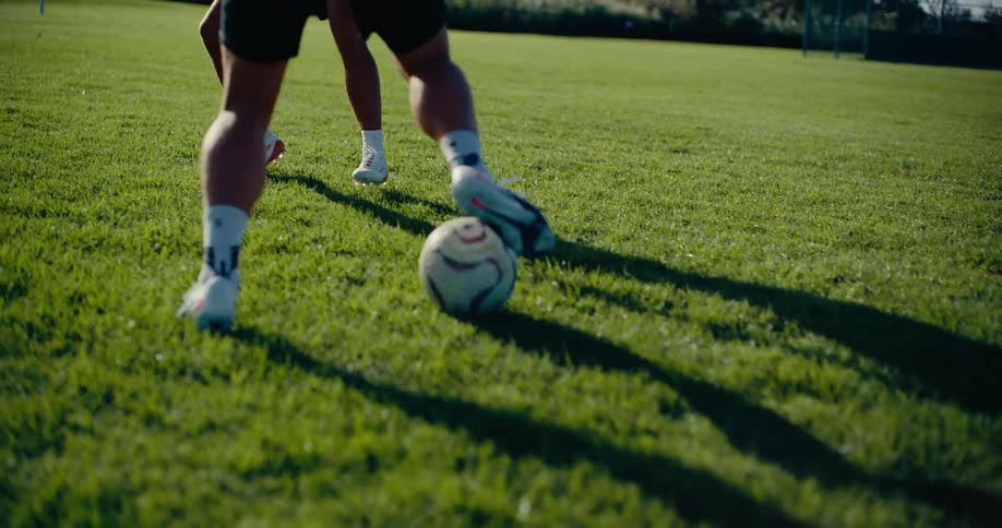 Two soccer players competing for the ball while dribbling on a grassy field at sunset