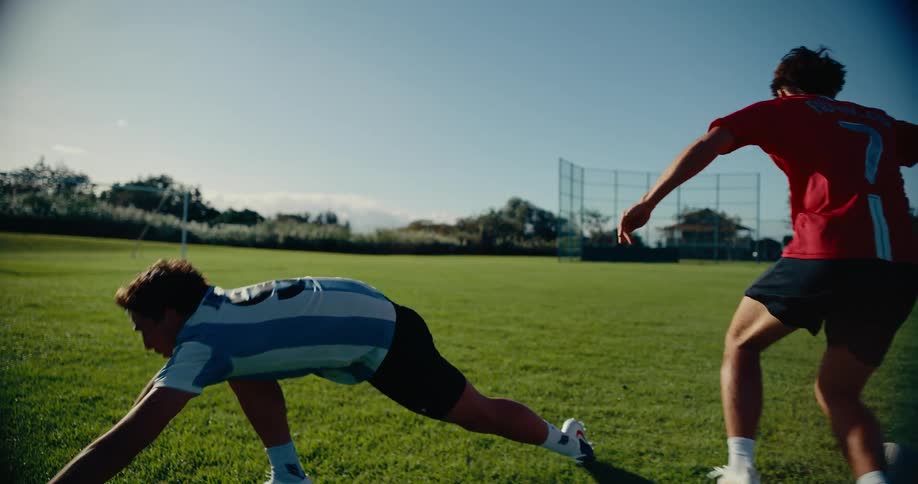 A player wearing a red ronaldo jersey dribbles past a defender in an argentina shirt on a sunny grass field after the defender falls while attempting a tackle the player in red continues down the field with the ball