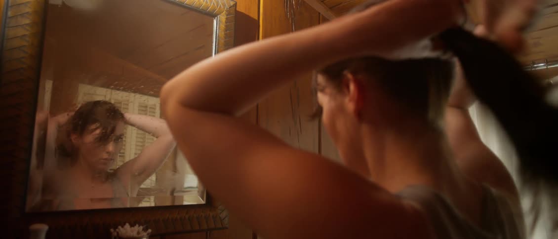 A woman wipes the fog off a bathroom mirror and begins doing her hair