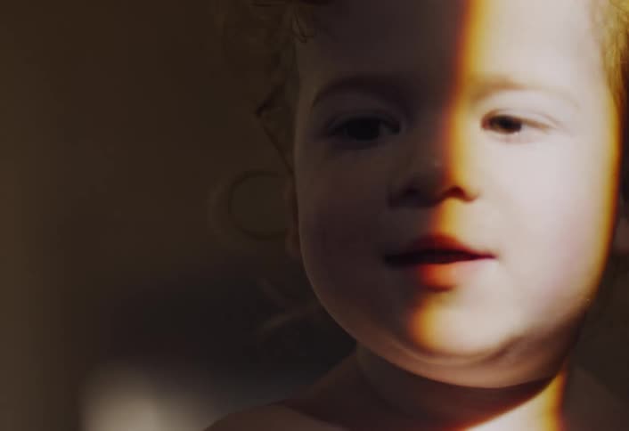 A smiling toddler looks ahead in a warm indoor setting with soft lighting and a blurred background