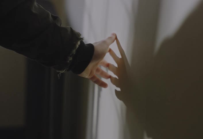 Hand with a ring extended casting a shadow on a lit wall