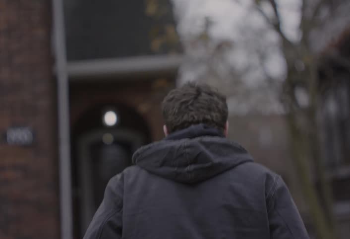 A young man is walking in a suburb area on a gloomy day he walks into a house on the street
