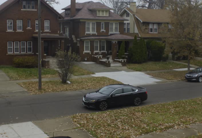 On a gloomy day on a residential street a black car drives up and parks at the curb