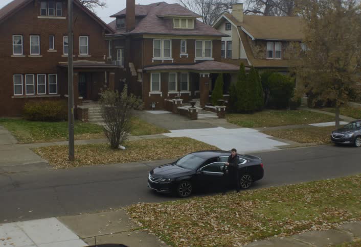 Man exits a car parked on a residential street and walks up a driveway on an autumn day