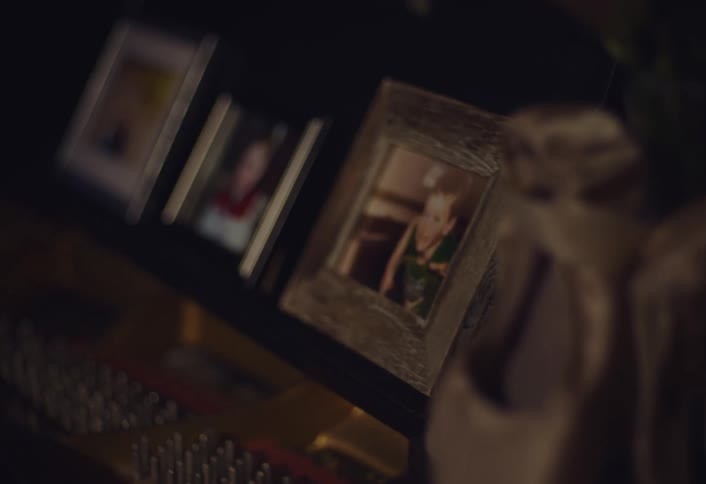 Closeup of framed family photos on a dimly lit shelf softly illuminated by warm light with a blurred background
