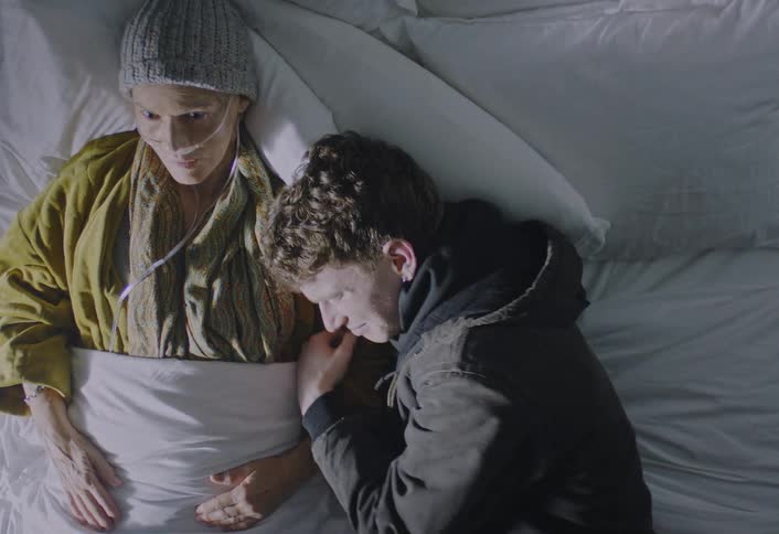 A man lies emotional and crying beside a patient during a quiet moment in a hospital bed