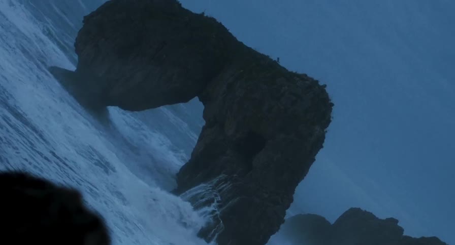 Powerful ocean waves crash around a large natural sea arch rock formation along a dark coastal shoreline