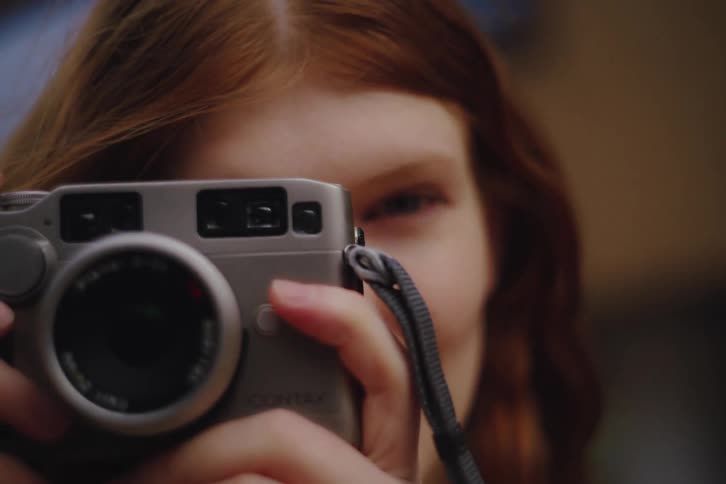 Closeup of a young woman pressing a camera to her face as she takes a photograph with shallow depth of field