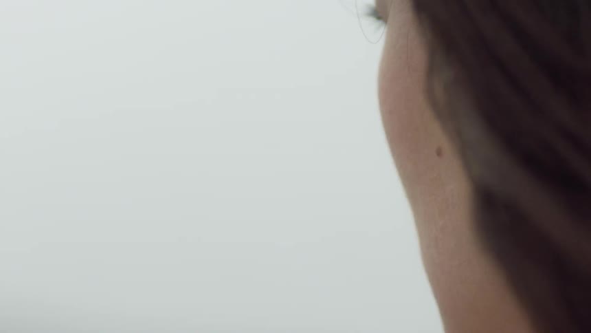 Woman stands looking off outside while snow flurries fall and wind blows