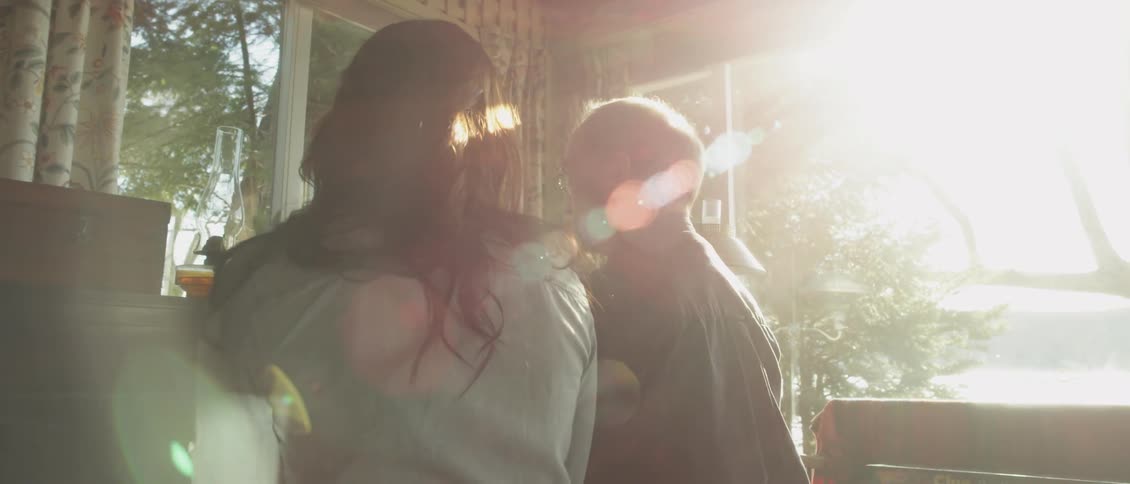 Two people sit under the light from the window by a piano