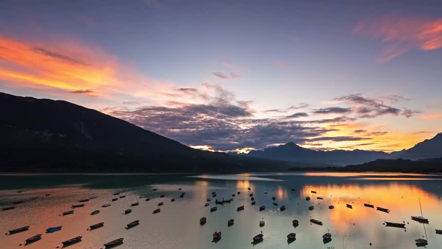 Boats anchored on a lake reflect sunset light between mountains