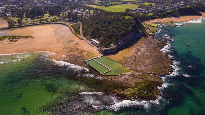 An aerial view shows a wide sandy beach and a river that flows into the ocean while the sun sets over the distant hills