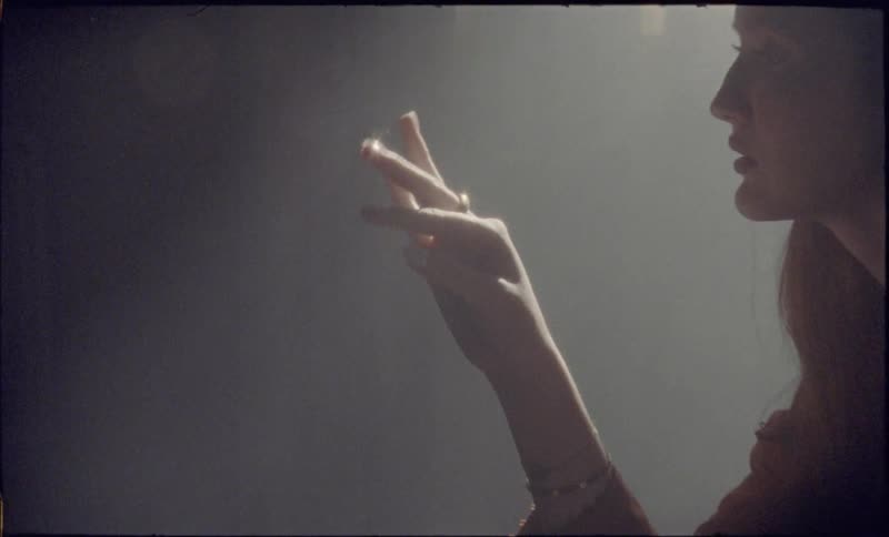 A woman looks at her fingers as they move in a smoky room