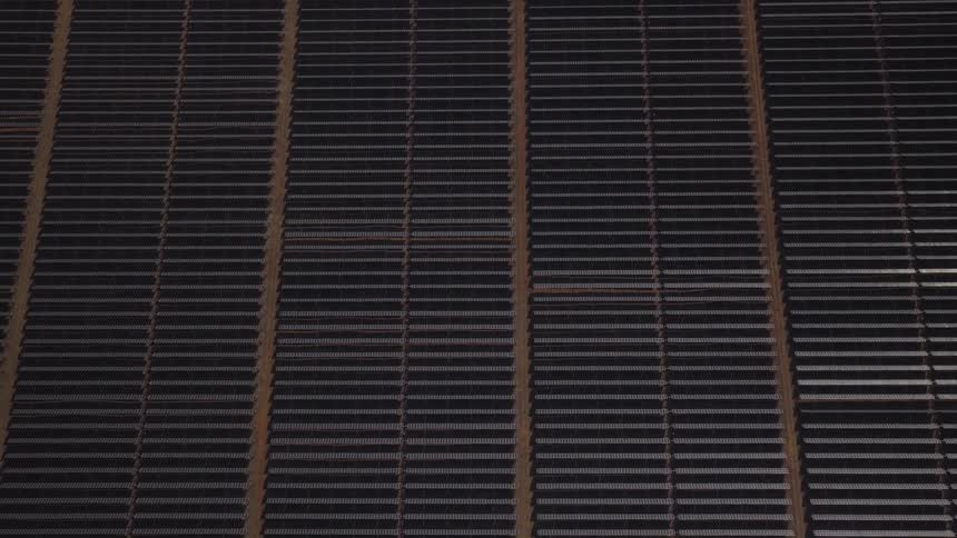 An overhead view shows long repeating rows of dark solar panels arranged in neat parallel lines