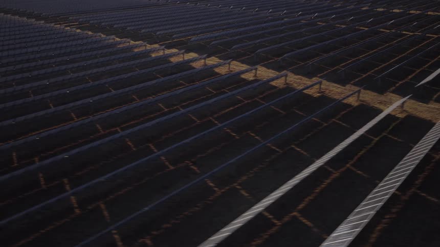 An aerial view shows a large field filled with long rows of solar panels