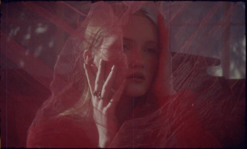 A woman poses indoors while covered in very thin and transparent fabric