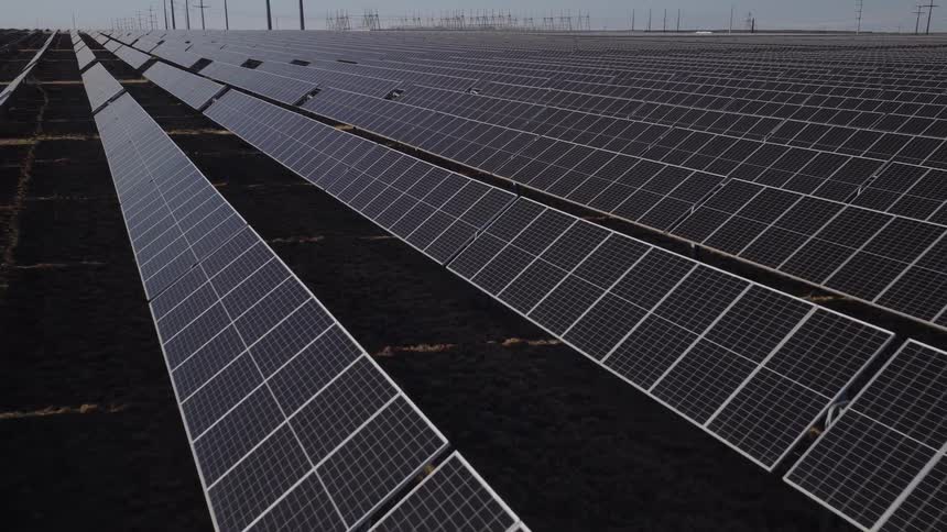 An aerial view glides over rows of solar panels in a large energy farm
