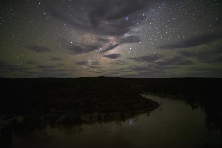 Clouds move across a starry sky over a river