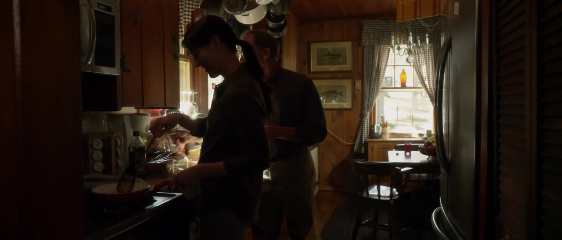 A man walks up to a woman cooking, and pours coffee