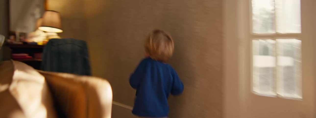 A child running around the living room having fun holding a bag while hiding behind a desk