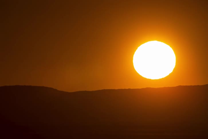 The glowing sun slowly rises behind the dark horizon casting a warm orange glow across the sky