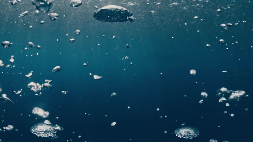 Underwater silhouette of a scuba diver rising through bubbles surrounded by a swirling school of fish