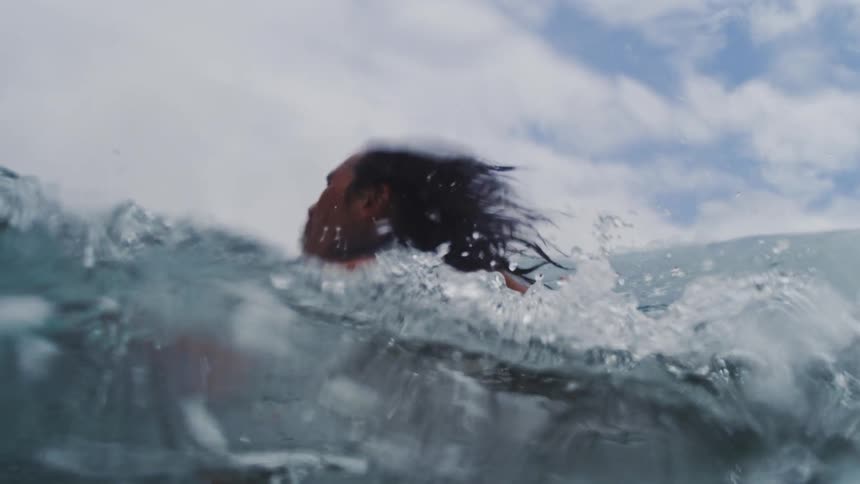 Person floats in the ocean as a nearby wave swells on a cloudy day
