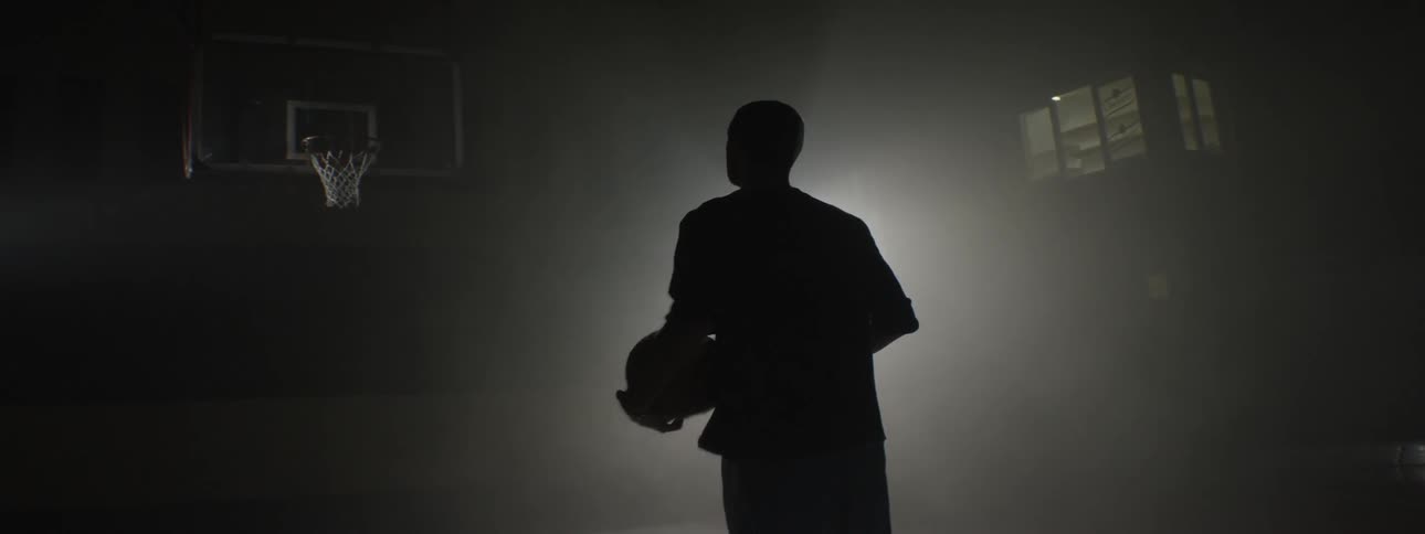 A light shining on a man who is playing basketball