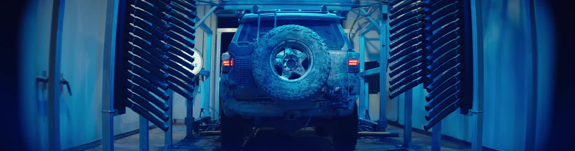 Dirty jeep driving through a car wash as the cleaning machines turn