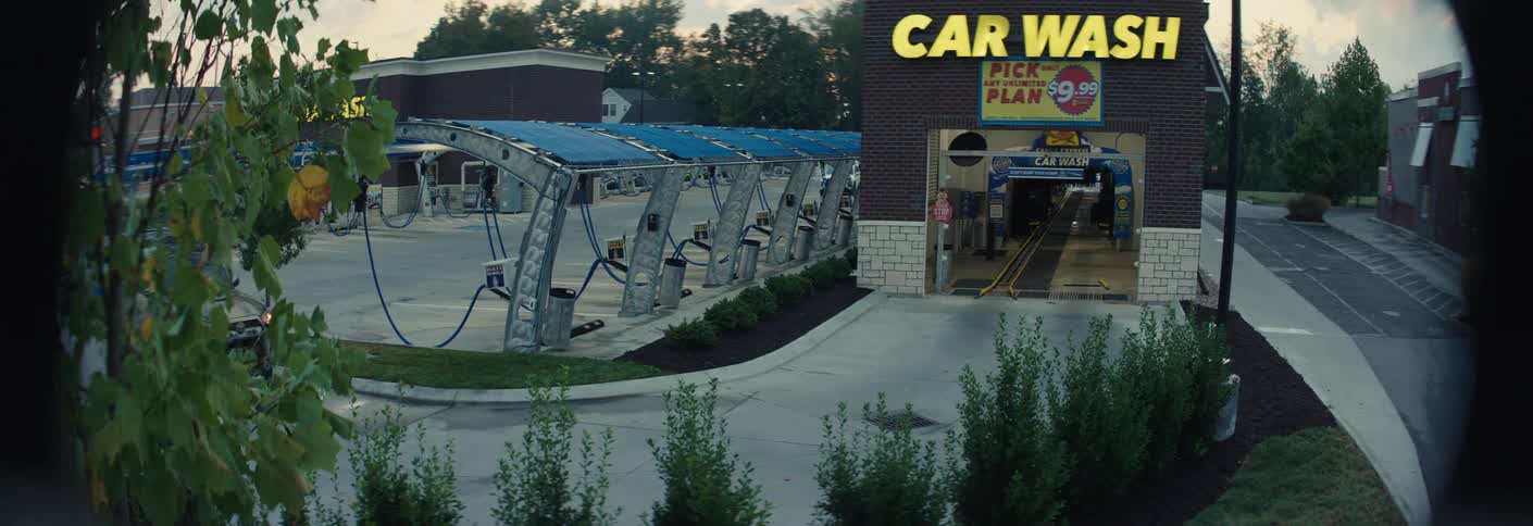 The video shows an outdoor car wash facility during the early evening or twilight hoursa mudcovered suv drives into the frame from the left and approaches the entrance of the car wash tunnel